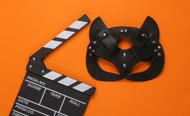 Leather bdsm mask of a cat with a clapperboard on an orange background. Cinema for adults, 18+