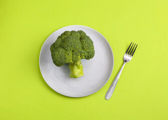 Broccoli on a plate with a fork, green background. Weight loss, healthy food concept