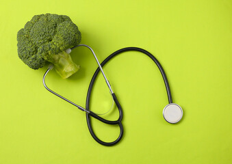Healthy food concept. Broccoli with stethoscope on green background. Top view