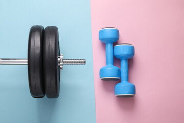 Obraz na płótnie Canvas Bodybuilding and fitness concept. Top view barbell composition with dumbbells on a blue-pink pastel background. Flat lay