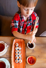 Little cute little boy eating sushi in a cafe, concept of eating. top view of child eating sushi...