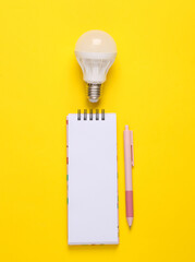 Idea's generator. Notepad with light bulb on yellow background
