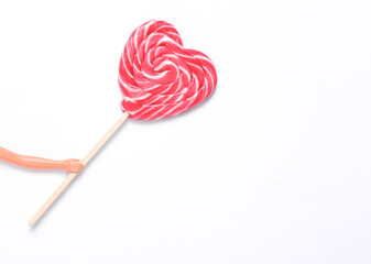The doll's hand holds a heart-shaped lollipop on white background. Minimal still life