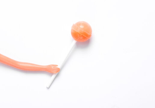 Doll hand holding lollipop on white background. Minimal halloween, junk food, sweets, concept. Top view