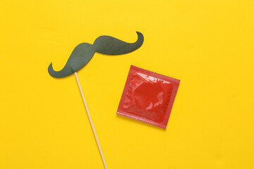 Mustache on stick, pack of condoms on yellow background