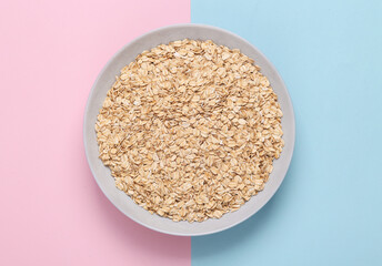 A plate of raw oatmeal on a blue pink pastel background. Healthy food concept.