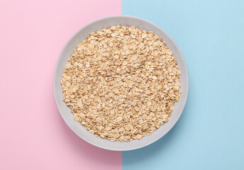 A plate of raw oatmeal on a blue pink pastel background. Healthy food concept.