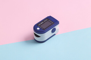 Electronic medical device pulse oximeter on a blue-pink pastel background. Measure the saturation...