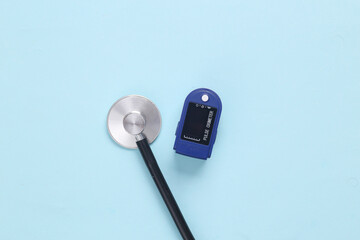 Medical devices for diagnosing health conditions. Pulse oximeter, stethoscope on a blue background. Top view