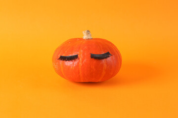Minimal halloween still life. Cute pumpkin with false eyelashes on orange background. Creative idea, beauty industry