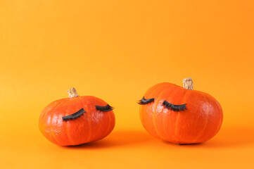 Minimal halloween still life. Two Cute pumpkins with false eyelashes on orange background. Creative idea, beauty industry