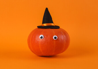 Pumpkin with goggles and a witch hat on orange background. Minimal halloween still life