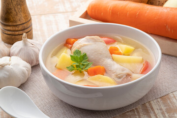 Clear chicken soup with potatoes carrot and onion in white bowl.Asian style food