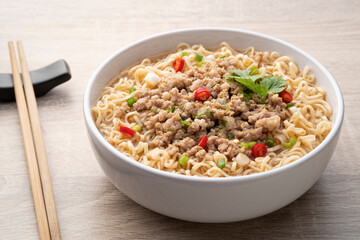 Instant noodle soup with minced pork in white bowl on wood table