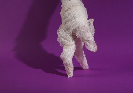 Mummy's hand steps fingers on a purple background with a shadow. Minimal halloween still life