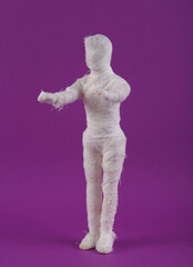 Mummy doll wrapped in bandages on a purple background. Minimal halloween concept