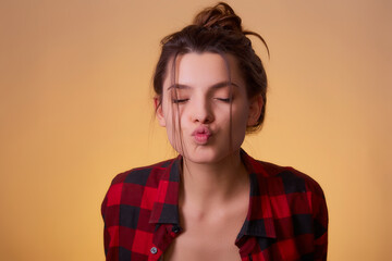 Fototapeta premium Portrait of funny childish woman send fun air kiss boyfriend valentine day date, celebration wear red n checkered shirt isolated over yellow background