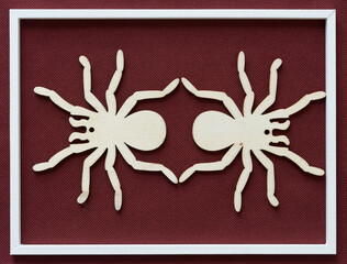 two wooden spider shapes on deep red brown fabric (framed in white)