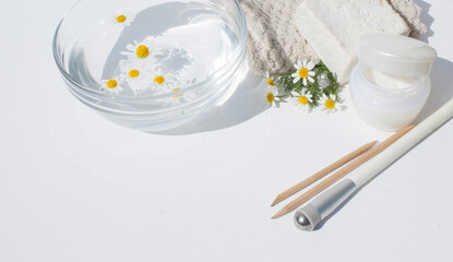Beauty concept. Cream , cosmetic accessories  and a glass transparent bowl with chamomile flowers on a white pastel background.Flat lay, top view, copy space