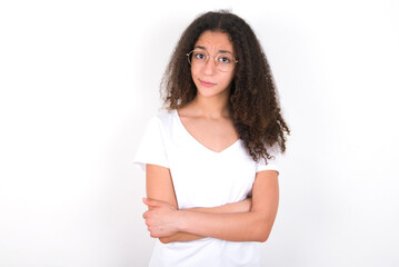 young beautiful girl with afro hairstyle wearing white t-shirt over white wall bitting his mouth and looking worried and scared crossing arms, worry and doubt.