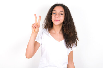 young beautiful girl with afro hairstyle wearing white t-shirt over white wall showing and pointing up with fingers number two while smiling confident and happy.