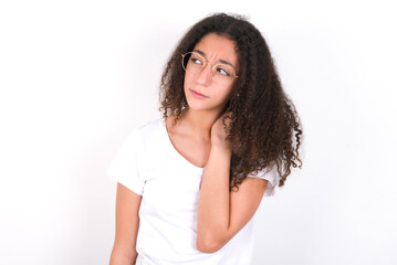 Fototapeta premium young beautiful girl with afro hairstyle wearing white t-shirt over white wall suffering from back and neck ache injury, touching neck with hand, muscular pain.