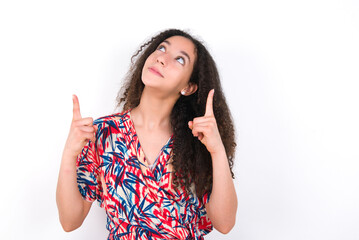 Successful friendly looking young beautiful girl with afro hairstyle wearing flowered dress exclaiming excitedly, pointing both index fingers up, indicating something.