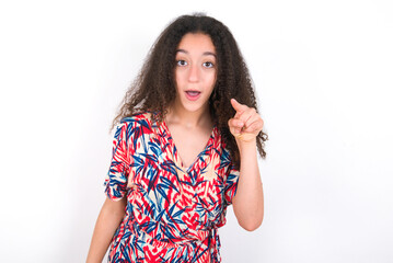 Shocked young beautiful girl with afro hairstyle wearing flowered dress points front with index finger at camera and. Surprise and advertisement concept.