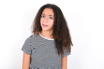 Fototapeta premium Portrait of dissatisfied young beautiful girl with afro hairstyle wearing striped t-shirt over whit smirks face, purses lips and looks with annoyance at camera, discontent hearing something unpleasant