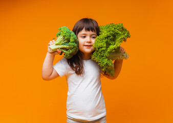 A little girl is holding a green raw broccoli and other vegetables on a yellow background.