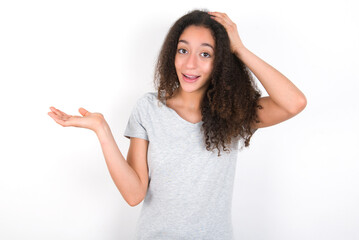 Shocked amazed surprised young beautiful girl with afro hairstyle wearing grey t-shirt over white wall hold hand offering proposition