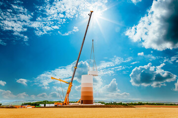 Building and assembling a construction windmill by crane. Farmland with construction work at the...