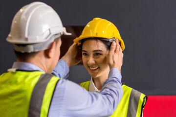 Man puts a safety helmet on woman at factory or plant site. Business heir concept. Happy lover...