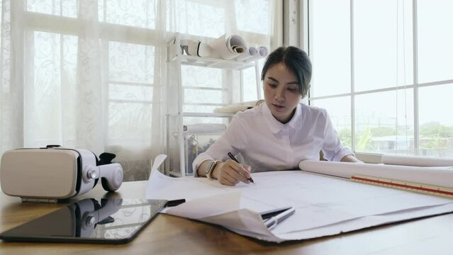 4K resolution slow motion, Asian female architect or engineer designer working with blueprint planning on workplace. Architect woman working in office.