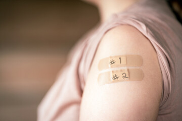 female with rolled up shirt sleeve to show the bandaids after the first two coronavirus vaccines...