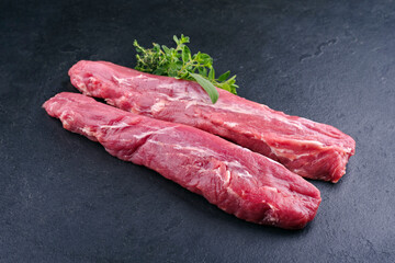 Traditional two raw duroc pork fillet pieces with herbs offered as close-up on a black board with...
