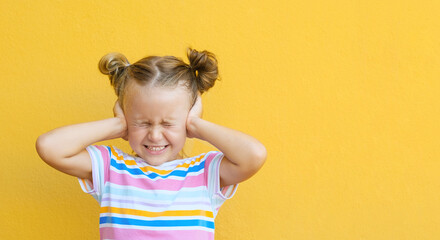 Unhappy little girl kid close eyes and cover ears hands being annoyed with noise wanting silence and calm atmosphere, isolated over yellow studio background