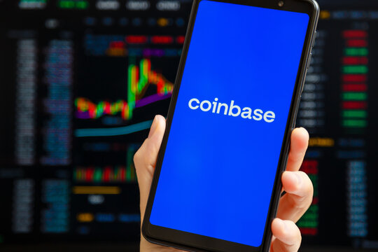 Ukraine, Odessa - October, 9 2021: Hand holding mobile with Coinbase app running at smartphone screen with trading page at background. Coinbase is American cryptocurrency exchange and trading platform
