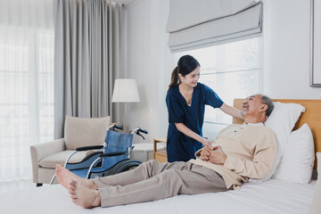 Senior Asian man laying on bed receives medical help for injury by Asian nurse, doctor woman assisting