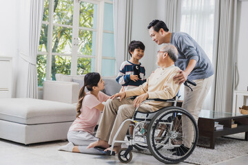 Happy family of senior with beautiful daughter, her husband and grandson take care old man sitting on wheelchair in house, positive dad have strength and positive thinking