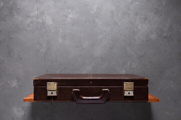 Old suitcase at shelf near wall. Shabby vintage suitcase