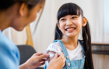 Childhood vaccination. Asian young woman doctor vaccinating little girl at home. Vaccine for...