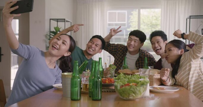 Happy hour diner at home relax smile look at camera shooting video photo on mobile app. Group of asia people young adult friend man and woman sit at dining table joy fun talk or eat food drink beer.