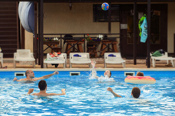 a group of people play ball in the water of the pool in the summer in hot weather
