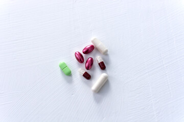 Pills and capsules in green, purple and brown on a white background.