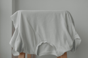 White t-shirt hanging on the chair with white background.