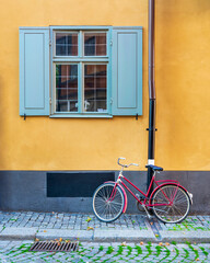 Fototapeta na wymiar Red bicycle parked under old vintage traditional window with blue shutters in an orange wall at a narrow cobblestone street in the old town of Gamla Stan, Stockholm, Sweden