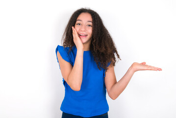 Crazy Teenager girl with afro hairstyle wearing blue T-shirt over white wall  advising discount...