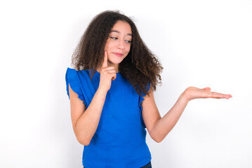 Funny Teenager girl with afro hairstyle wearing blue T-shirt over white wall  holding open palm new product. I wanna buy it!