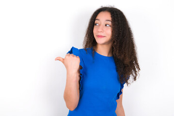 Charming Teenager girl with afro hairstyle wearing blue T-shirt over white wall  looking at copy space having advertisements